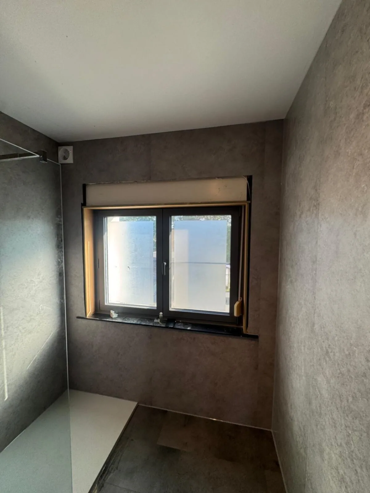 Badkamer rondom bekleed met grijze steenlook wandpanelen, raam en inloopdouche
