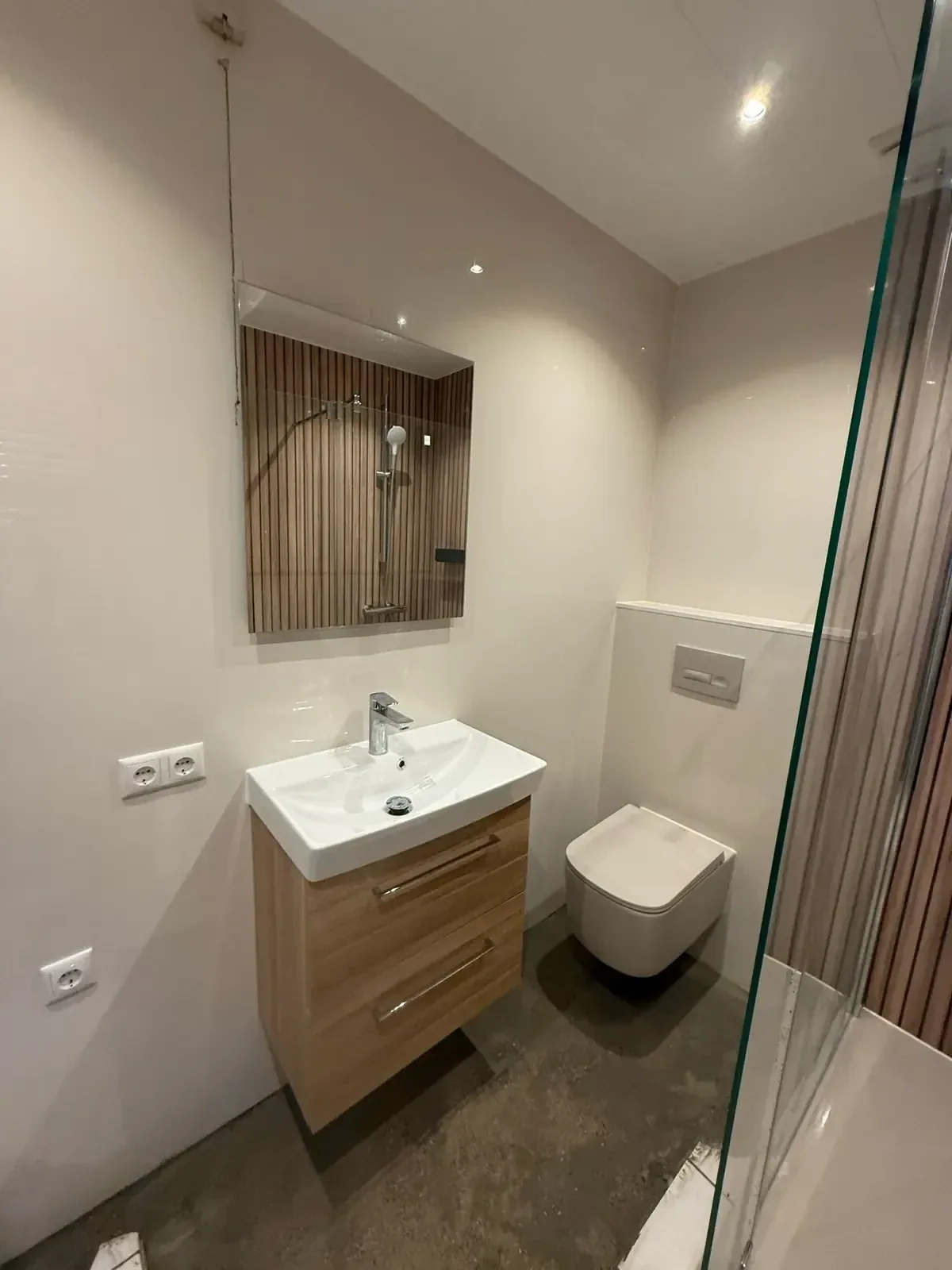 Houten wastafelmeubel met spiegel en hangtoilet in een lichte badkamer met lamellenwand