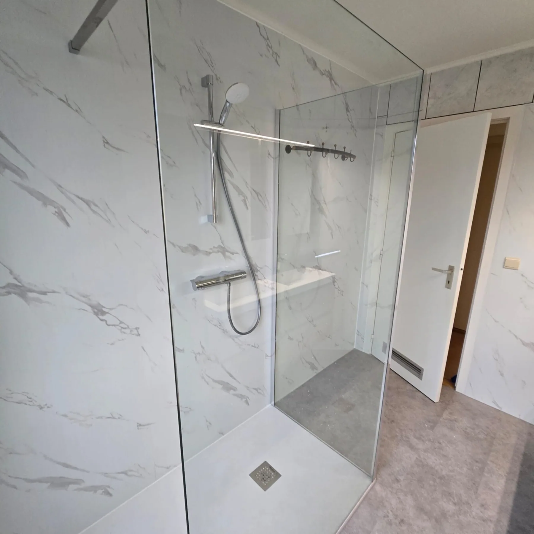 Ruime inloopdouche met glazen wand, thermostaatkraan en witte marmerlook wandpanelen
