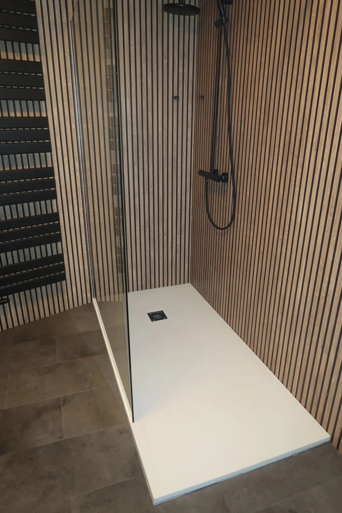 Inloopdouche met witte douchebak, zwarte regendouche en houtlook lamellenpanelen