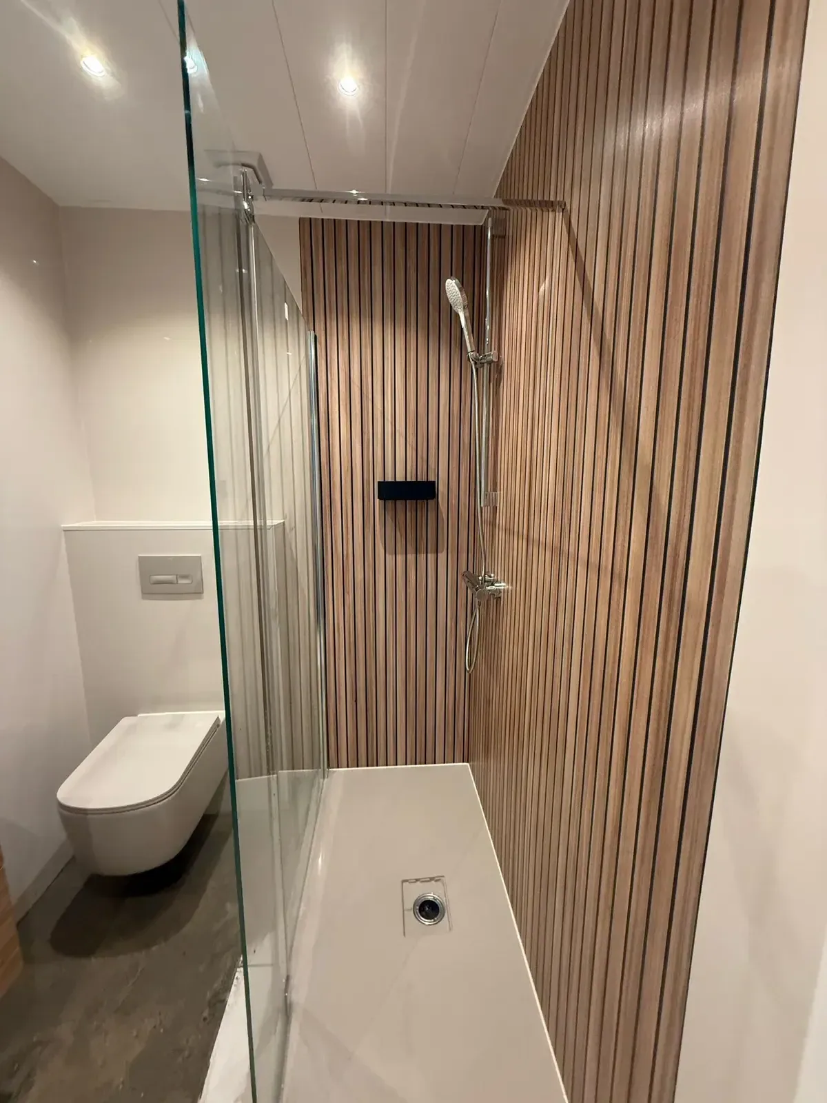 Inloopdouche met glazen wand en houtlook lamellenwand, wit hangtoilet ernaast