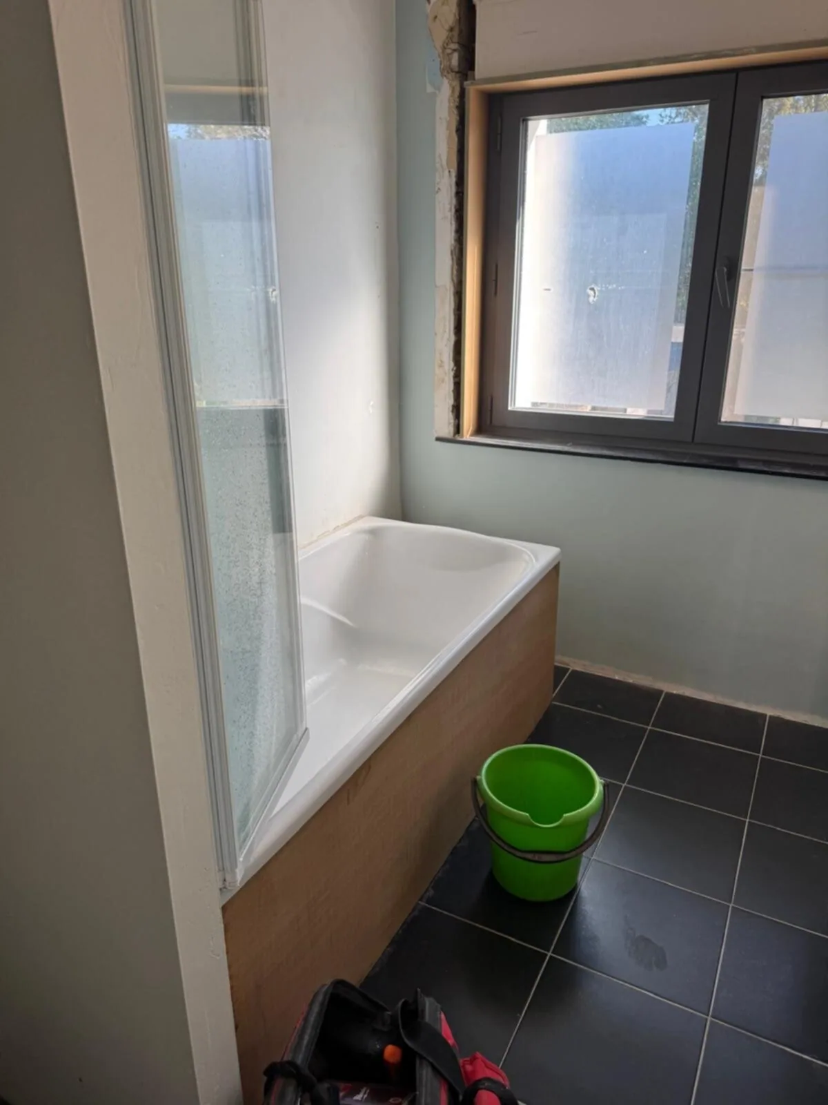 Oude badkamer met ligbad en badwand onder het raam, zwarte vloertegels