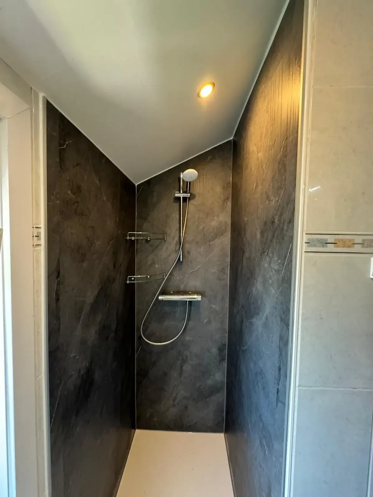 Smalle douche met donkere marmerlook panelen onder schuin plafond met inbouwspot