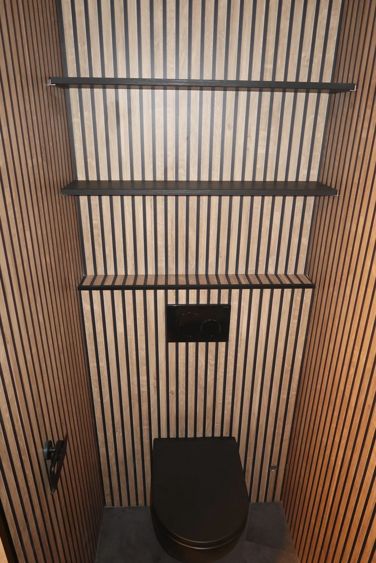 Toilet met houtlook lamellenwanden, zwart hangtoilet, zwarte bedieningsplaat en zwarte wandplanken