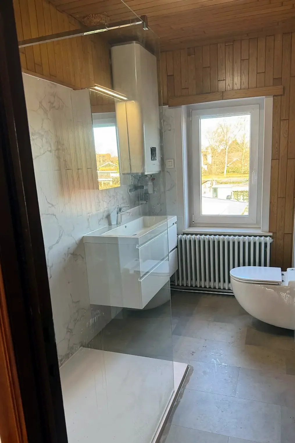 Dezelfde badkamer met lichte wandpanelen, wastafelmeubel en hangtoilet