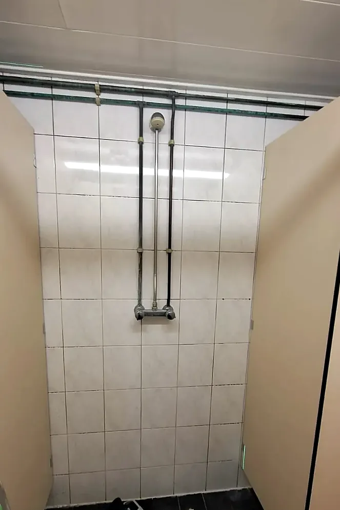 Douche met witte wandtegels en opbouwleidingen