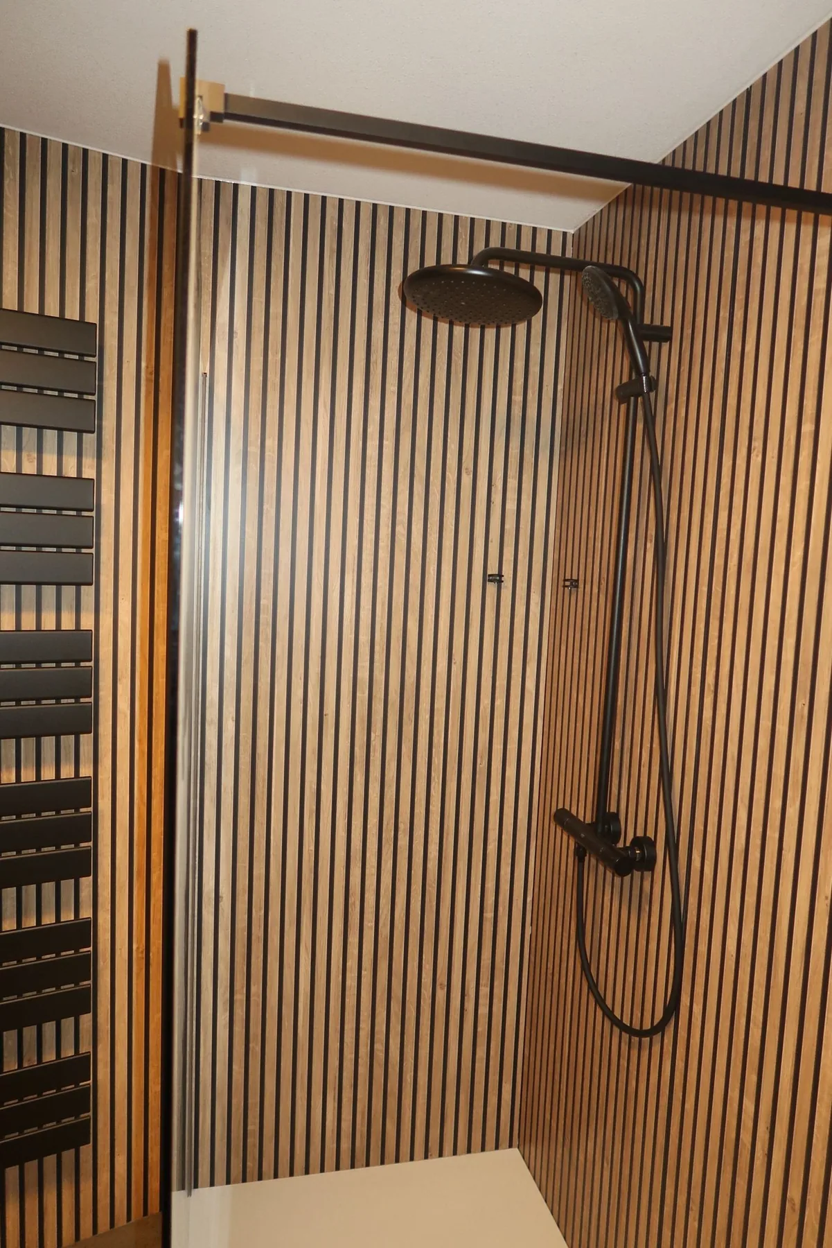 Zwarte regendouche met thermostaatkraan op een houtlook lamellenwand